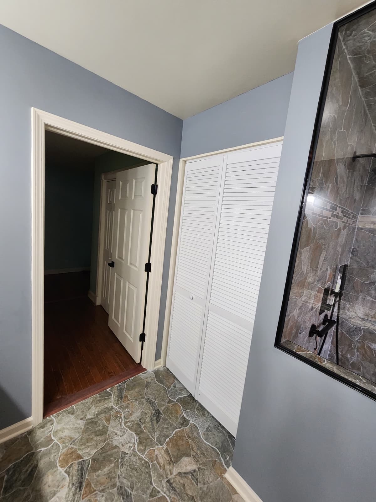 Blue-walled bathroom with white louvered closet and a framed stone shower.