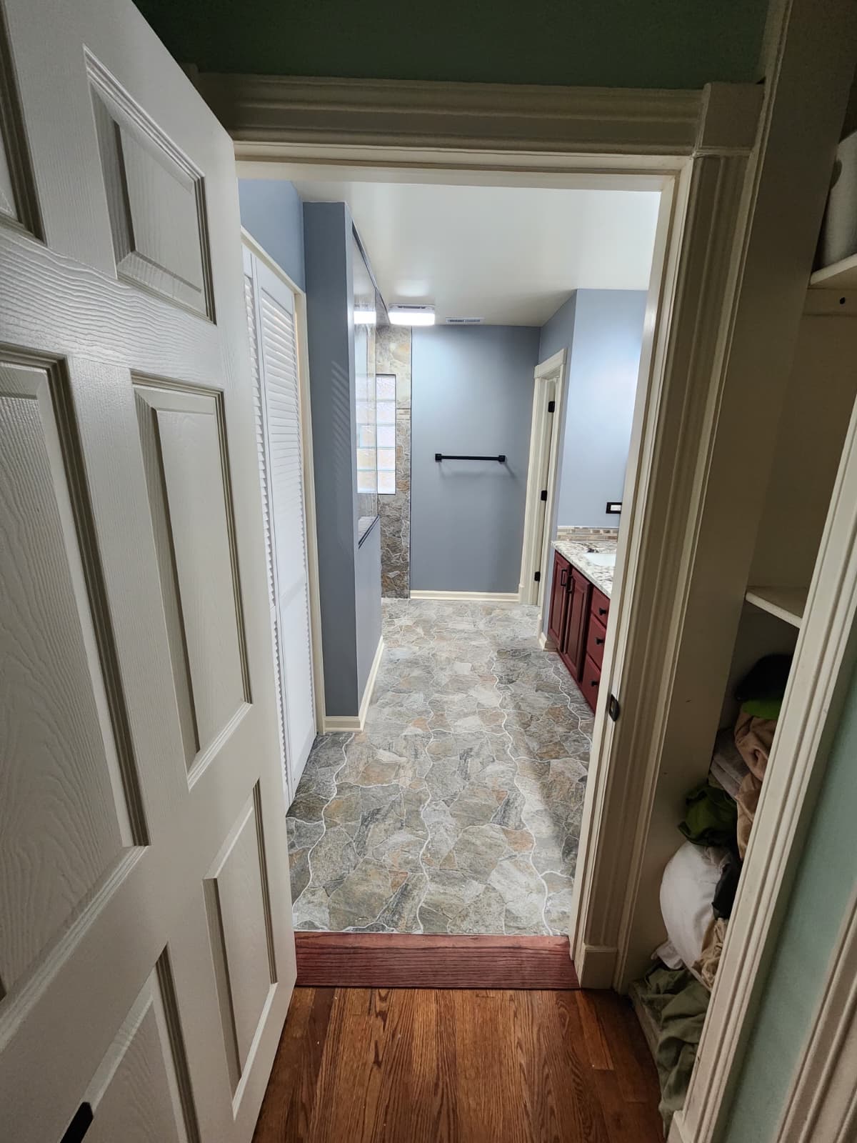 Blue-walled bathroom hallway with natural stone floor and vanity beyond.