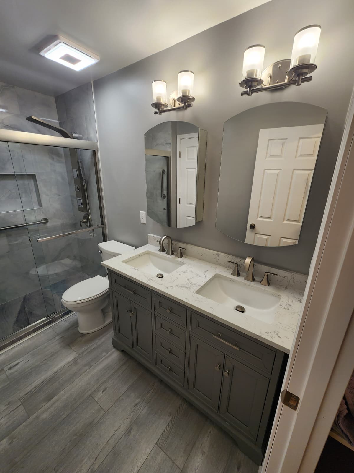 Gray double vanity with quartz counter, framed glass shower, and gray marble tile.