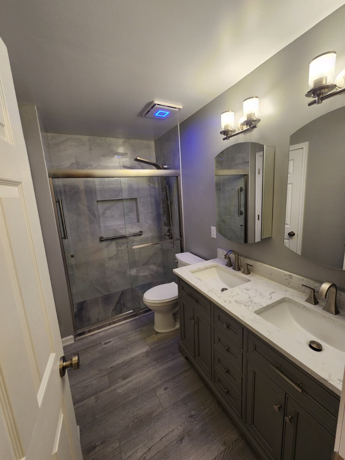 Gray double-vanity bathroom with gray marble shower and blue accent lighting.