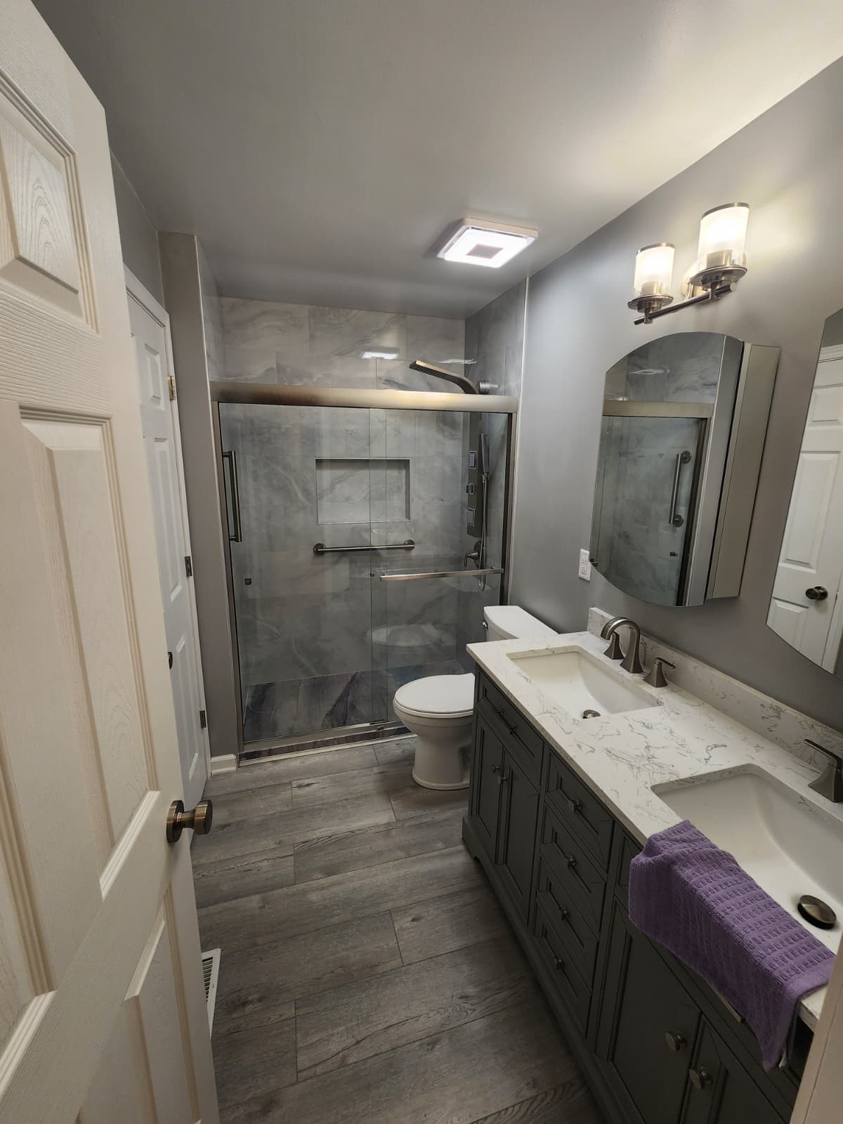 Gray double-vanity bathroom with marble-look shower and wood-look plank floor.