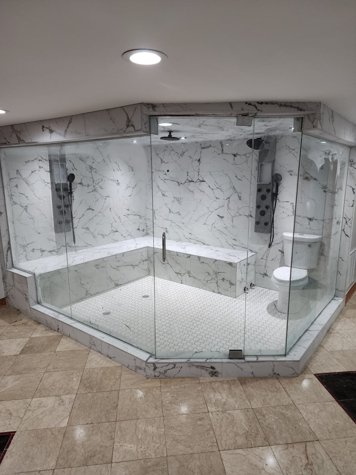 White marble corner shower enclosure with dual rainfall heads, body jets, and a tiled bench.