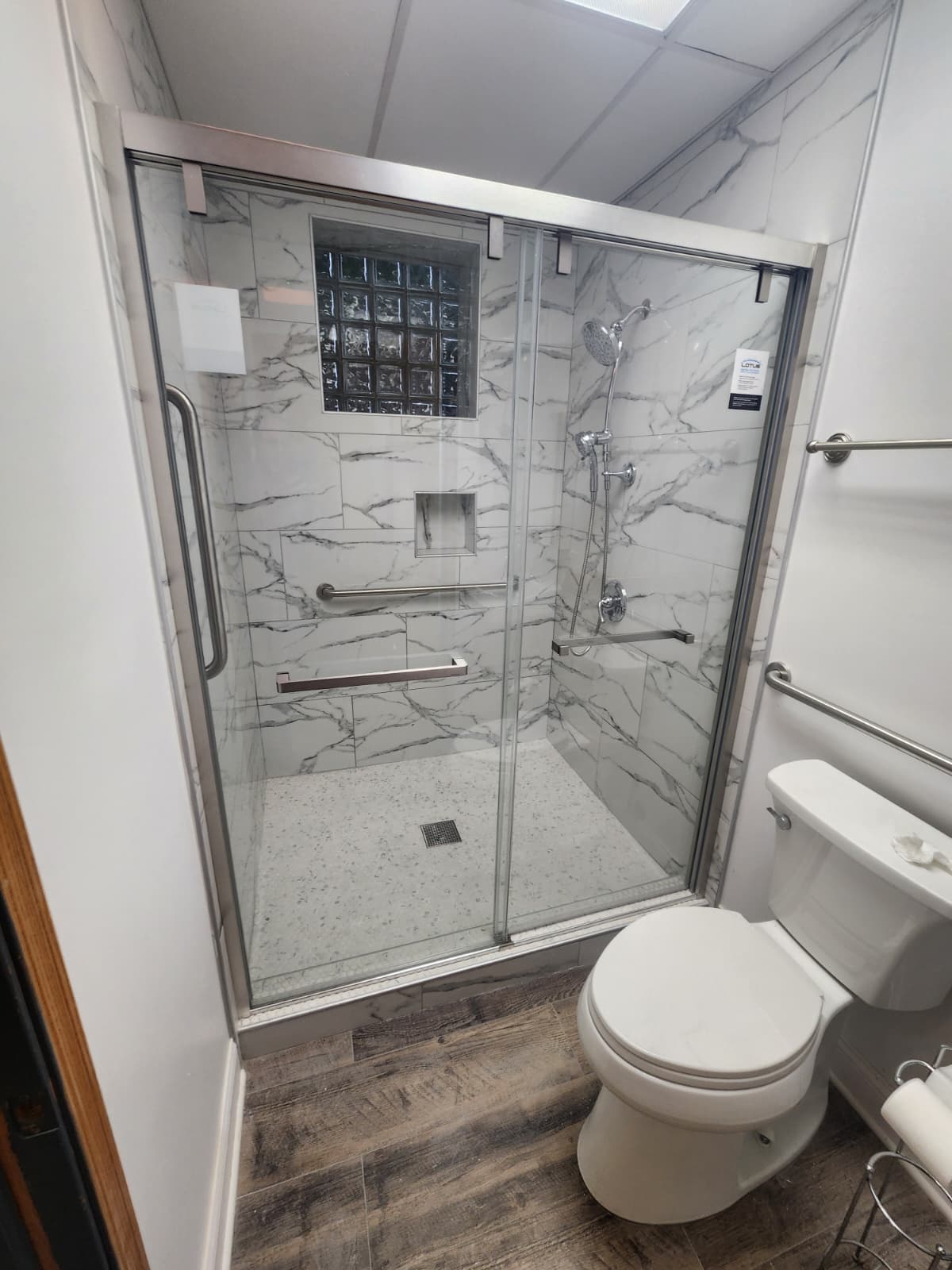 White marble walk-in shower with sliding glass door and stainless grab bars for accessibility.