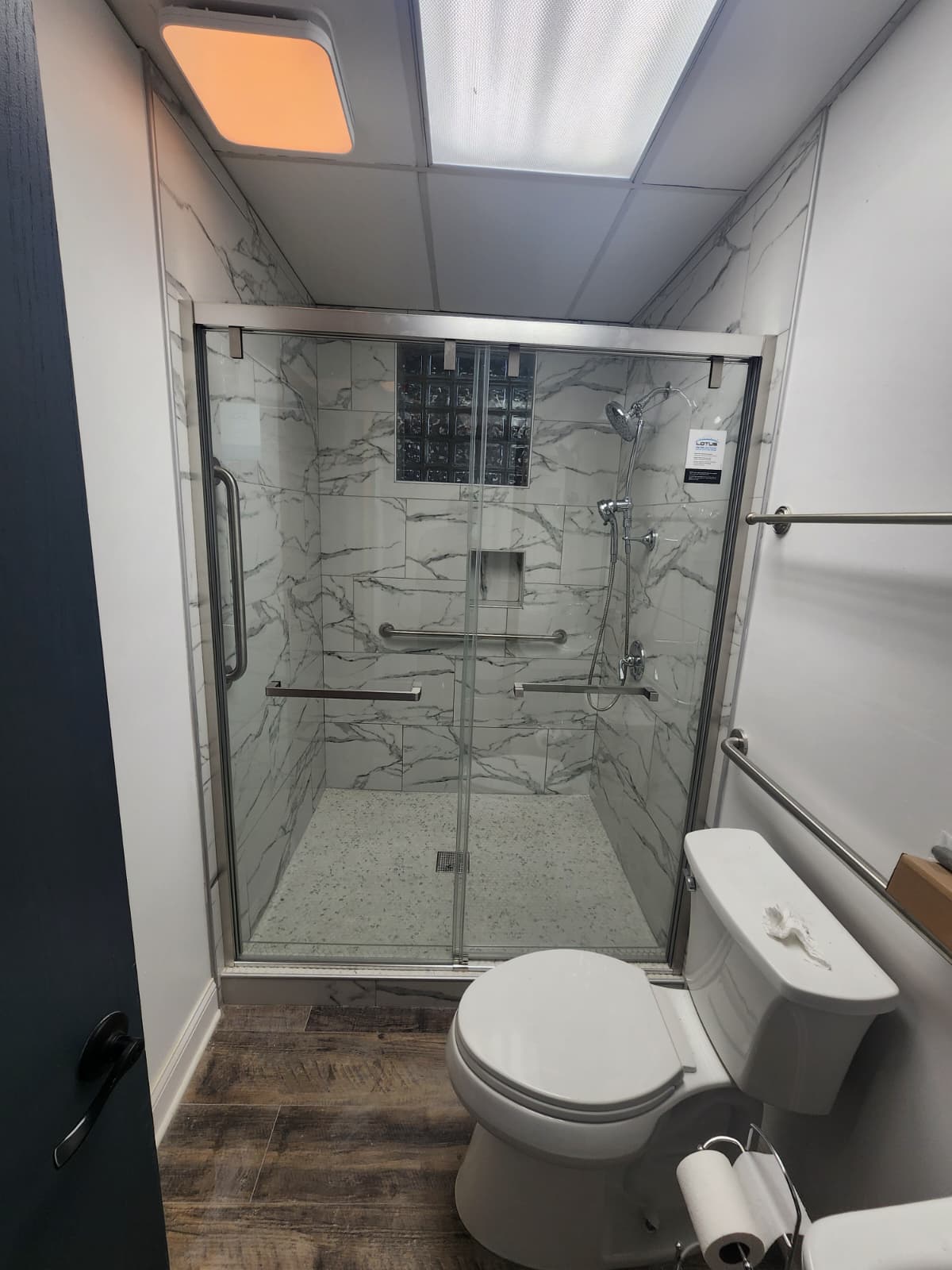 Marble-look walk-in shower with glass-block accent window and grab bars.
