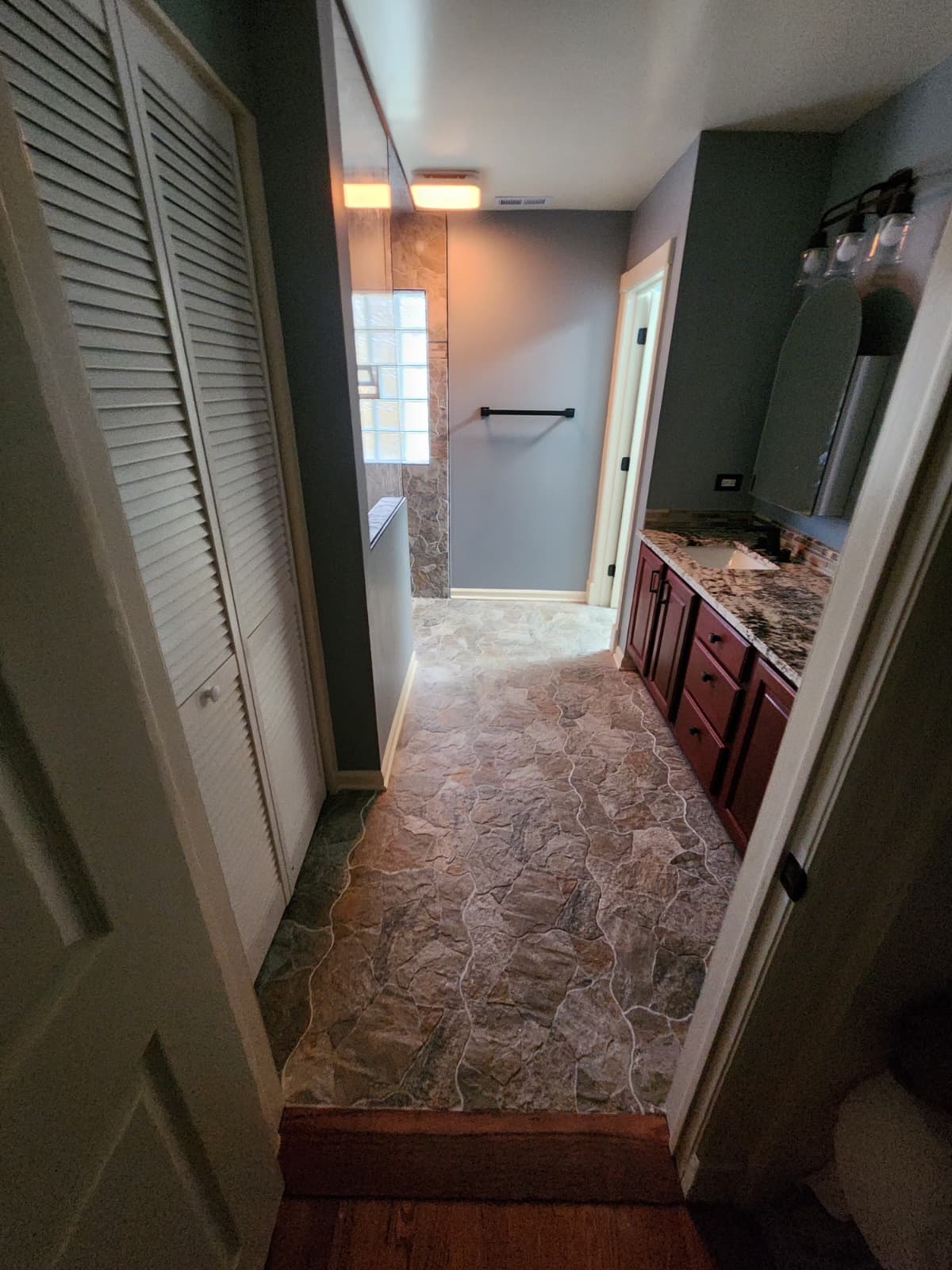 Stone-tiled bathroom hallway leading to a red-wood vanity with granite top.