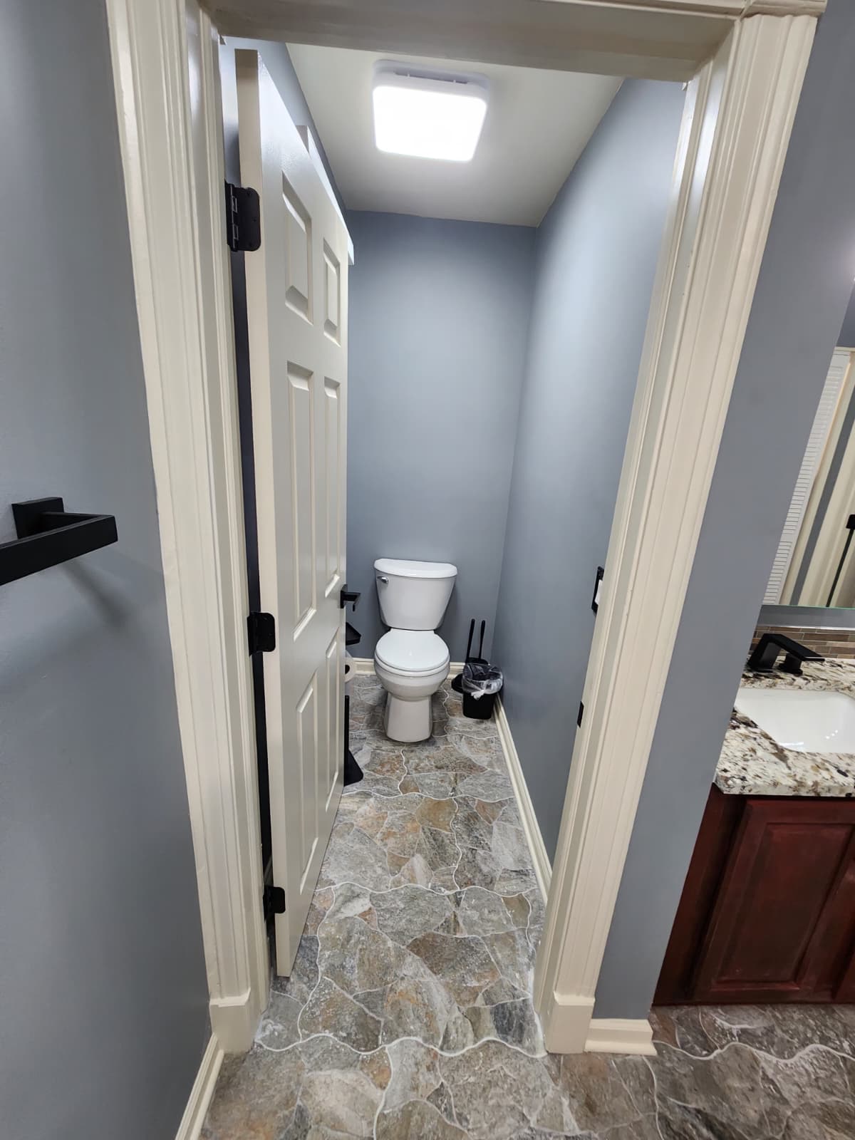 Toilet nook with stone floor tile beside a granite-topped vanity.