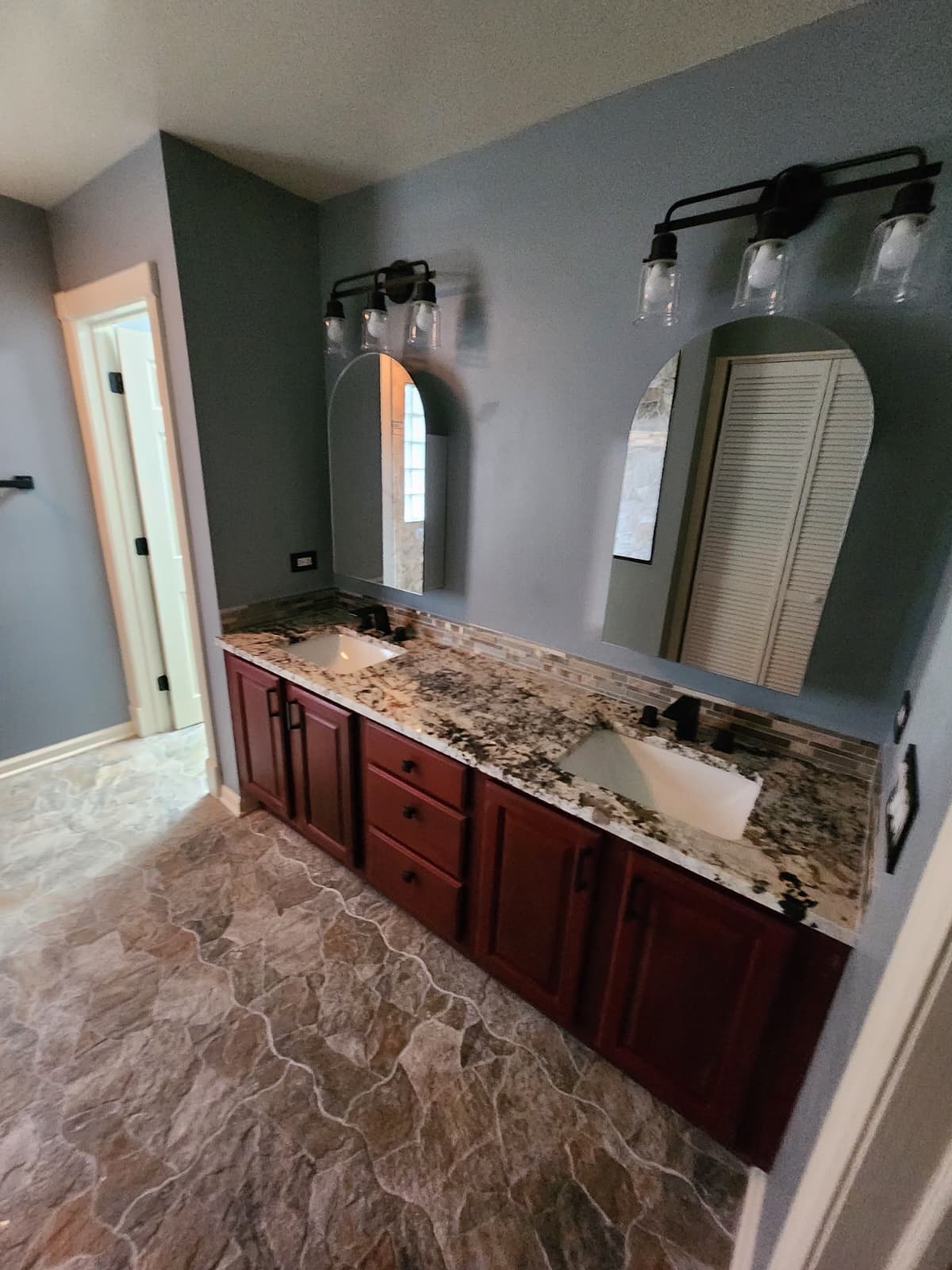 Red-wood double vanity with granite counter, arched mirrors, and natural stone floor.