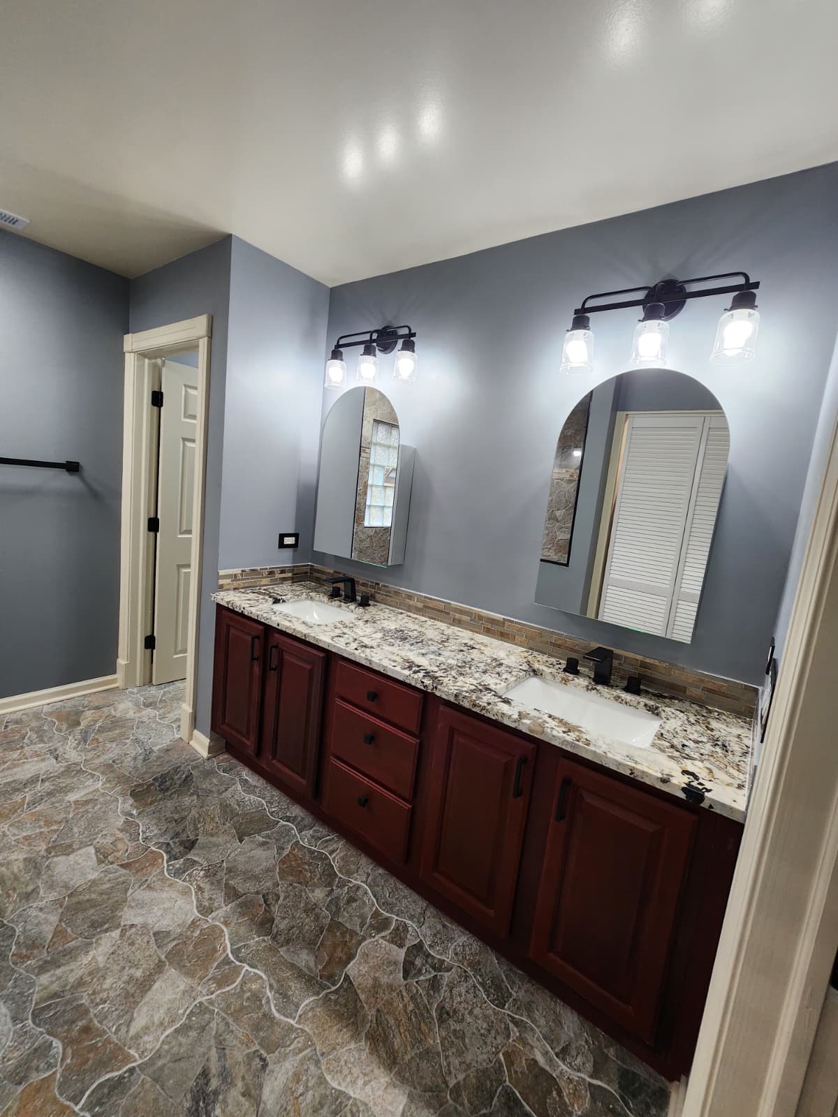 Red-wood double vanity with granite top and arched mirrors under bronze lighting.