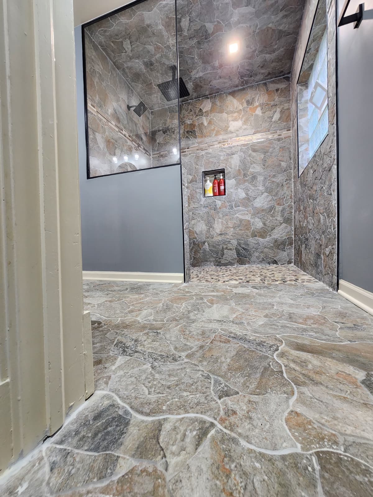 Natural stone walk-in shower and matching stone floor tile with a pebble shower base.