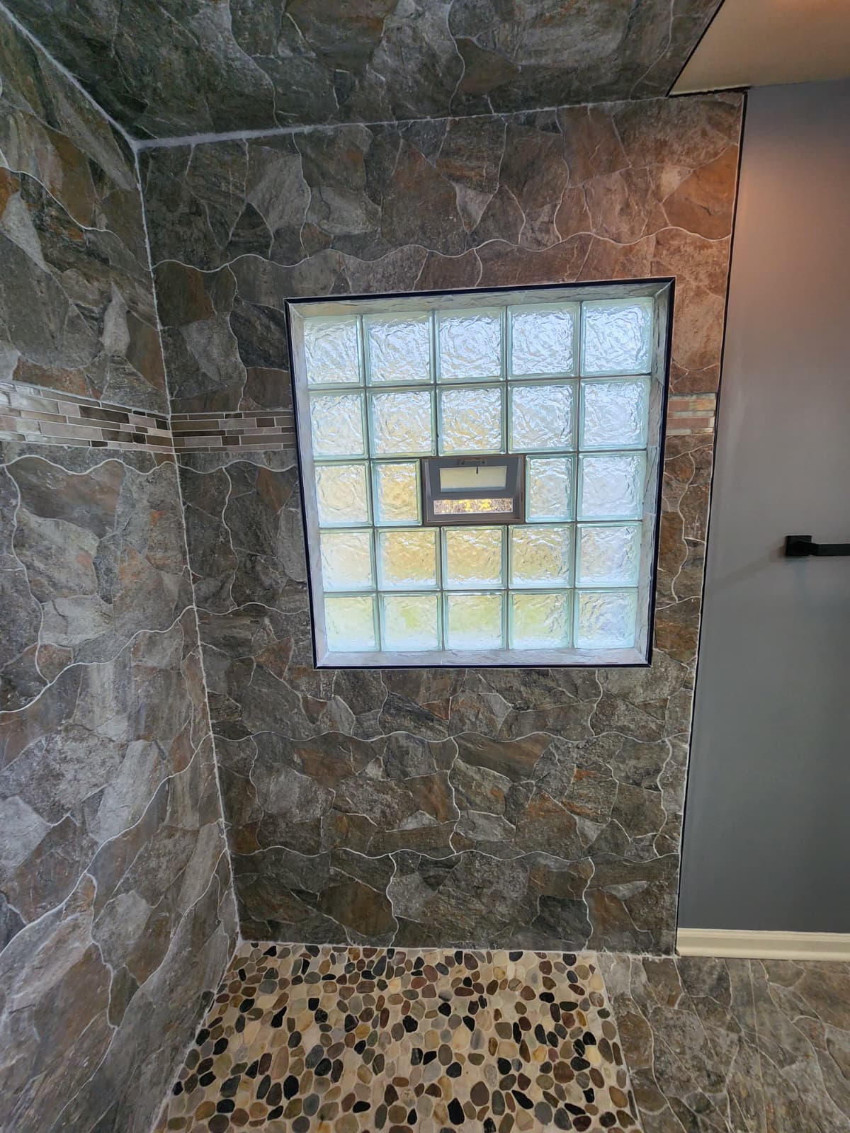 Stone-tiled shower with glass-block window and pebble floor accent.