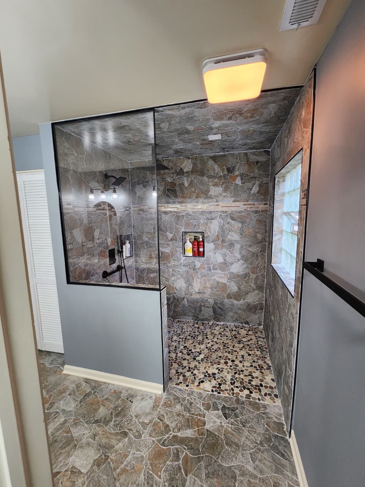Natural stone walk-in shower with half-glass wall and amber accent lighting.