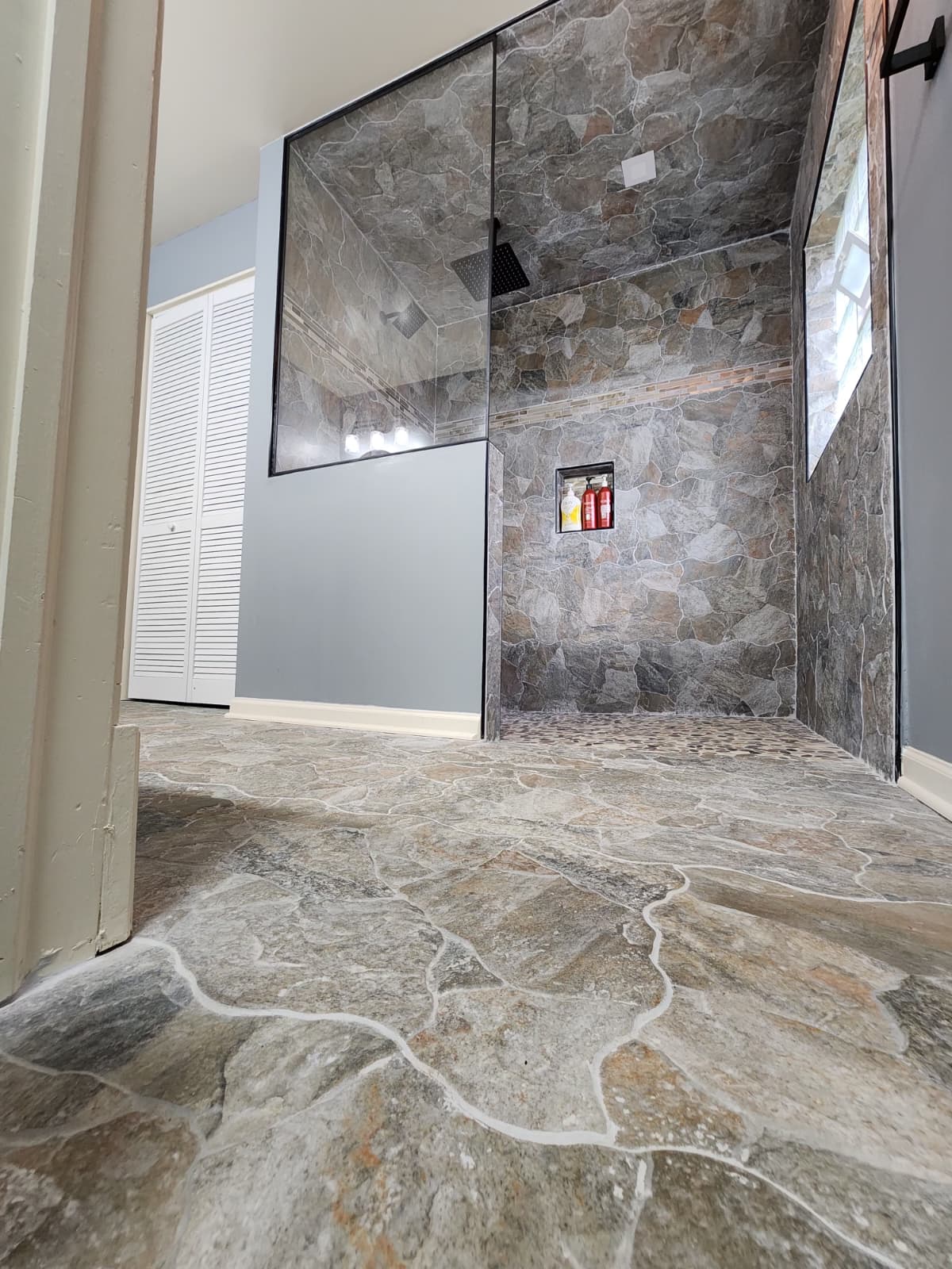 Stone shower and floor with niche storage, viewed from the bathroom entry.