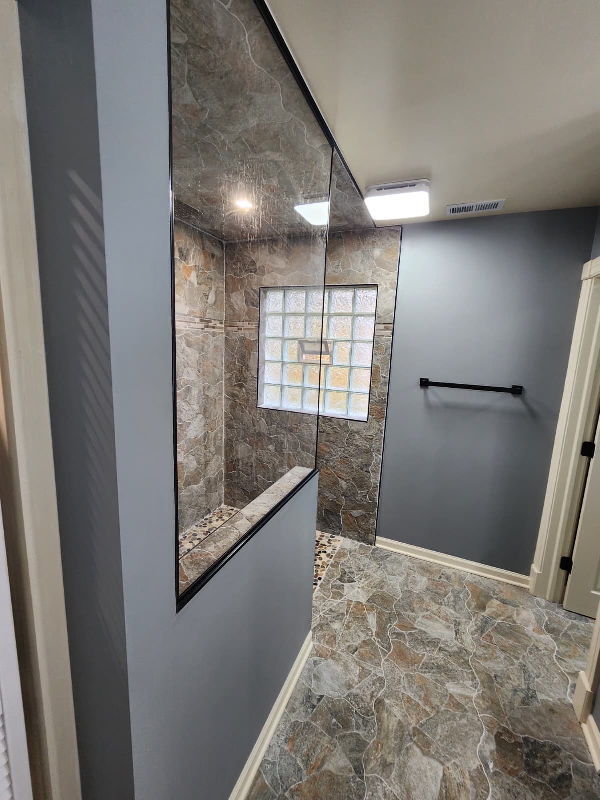 Stone-tiled shower with half-wall glass partition beside a white louvered closet.