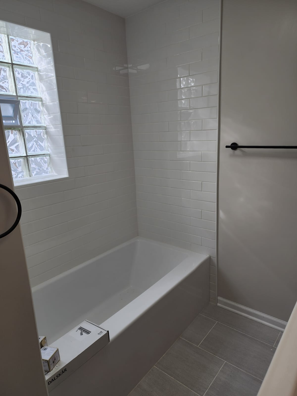 White subway-tile tub surround with glass-block window and matte black towel bar.
