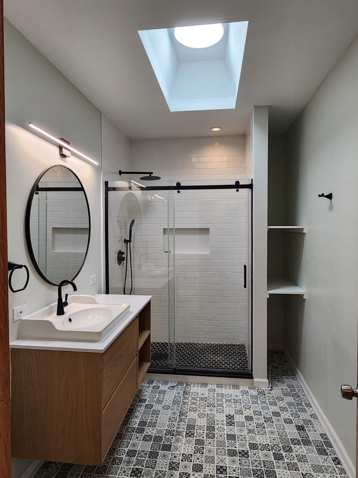 Walk-in glass shower with white subway tile and patterned cement floor tile, with floating wood vanity.