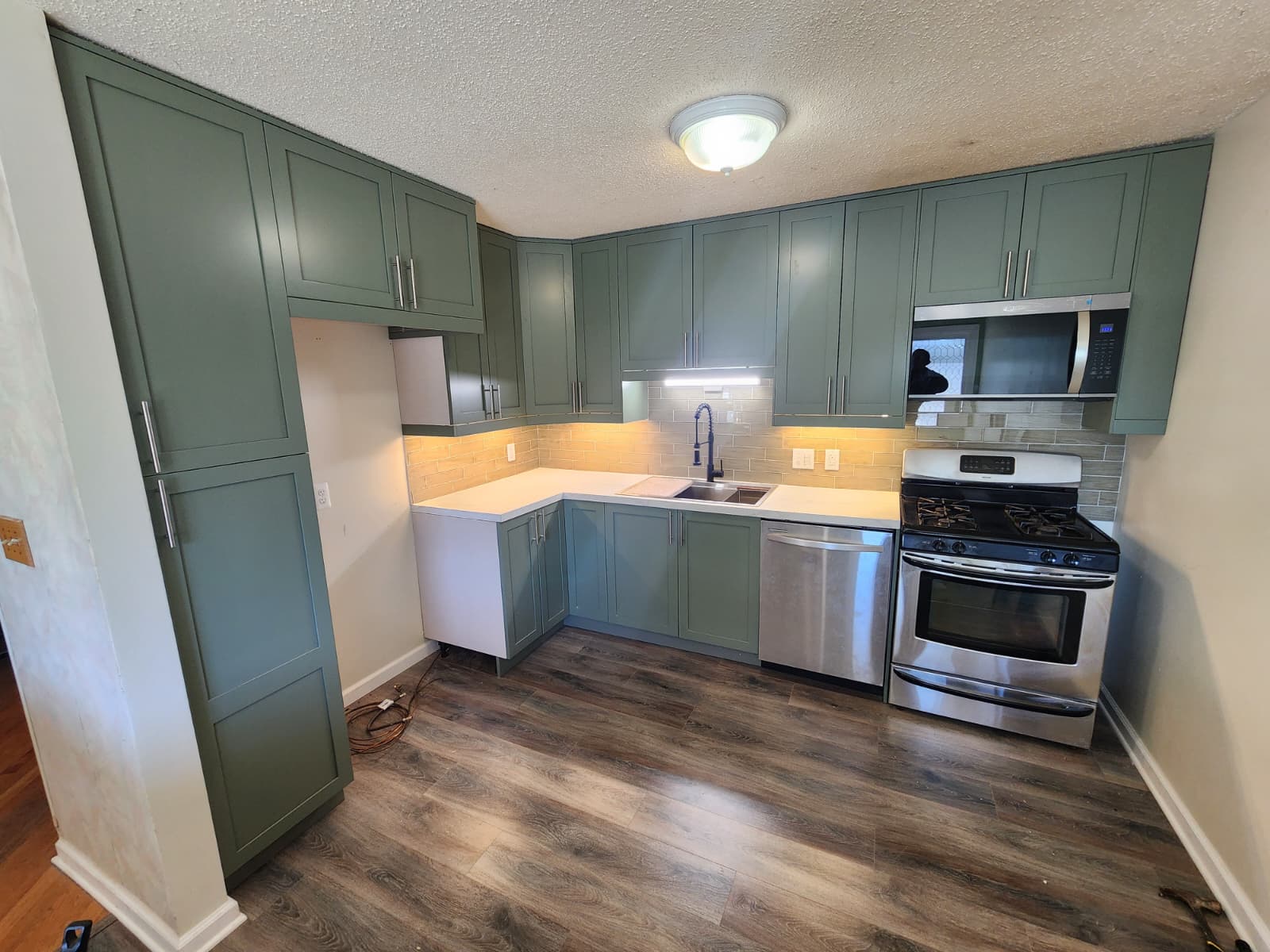 Green shaker-cabinet kitchen, L-shaped layout, with stainless range and dishwasher.