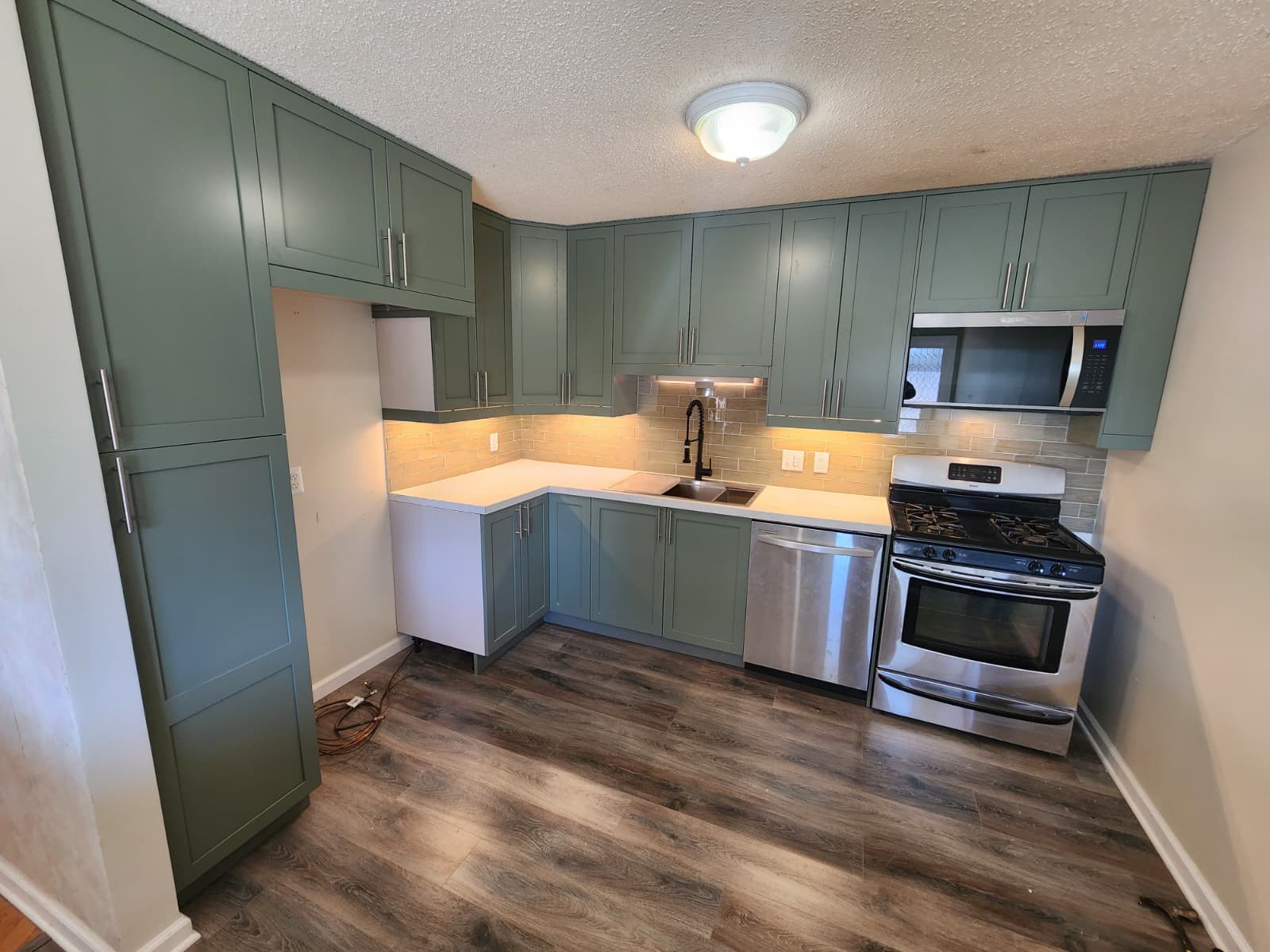 Green-cabinet kitchen corner with farmhouse-style faucet and tile backsplash.