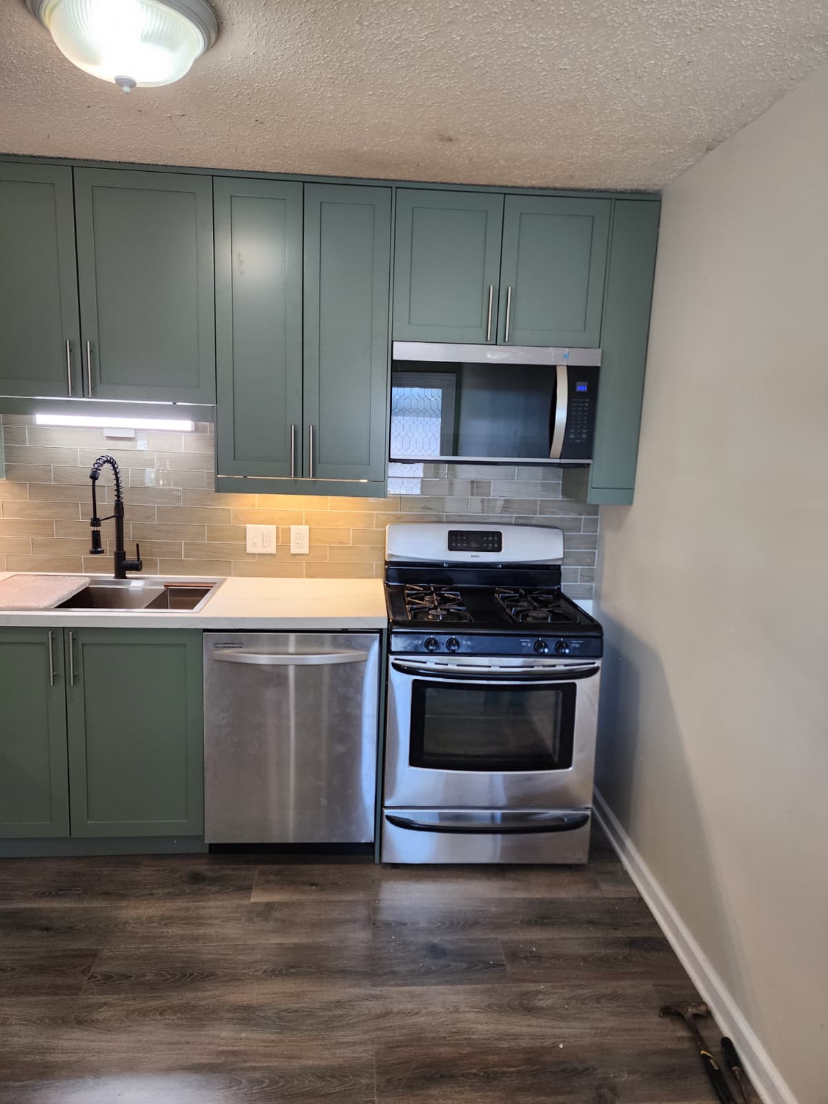 Close view of a green-cabinet kitchen with stainless gas range and over-range microwave.